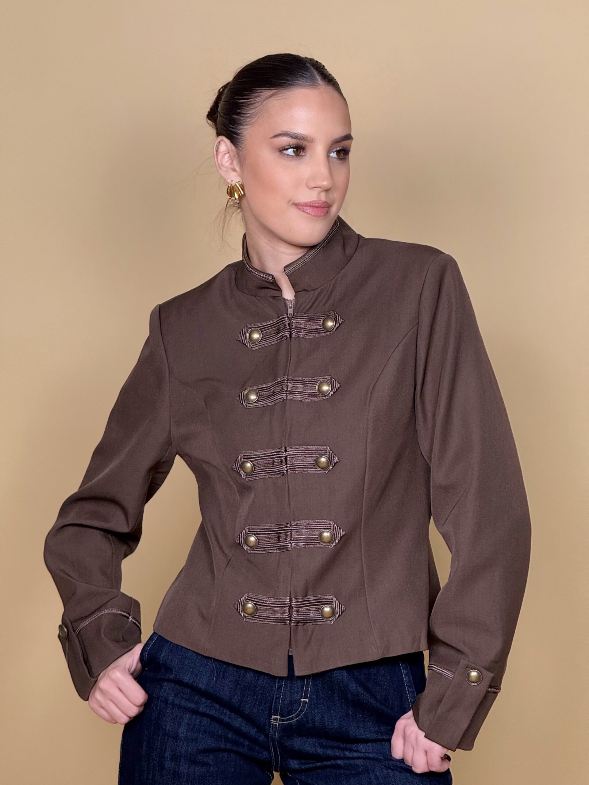 Model nosi žensku military jaknu Imperial Mocha kratkog kroja s visokim ovratnikom i ukrasnim gumbima.