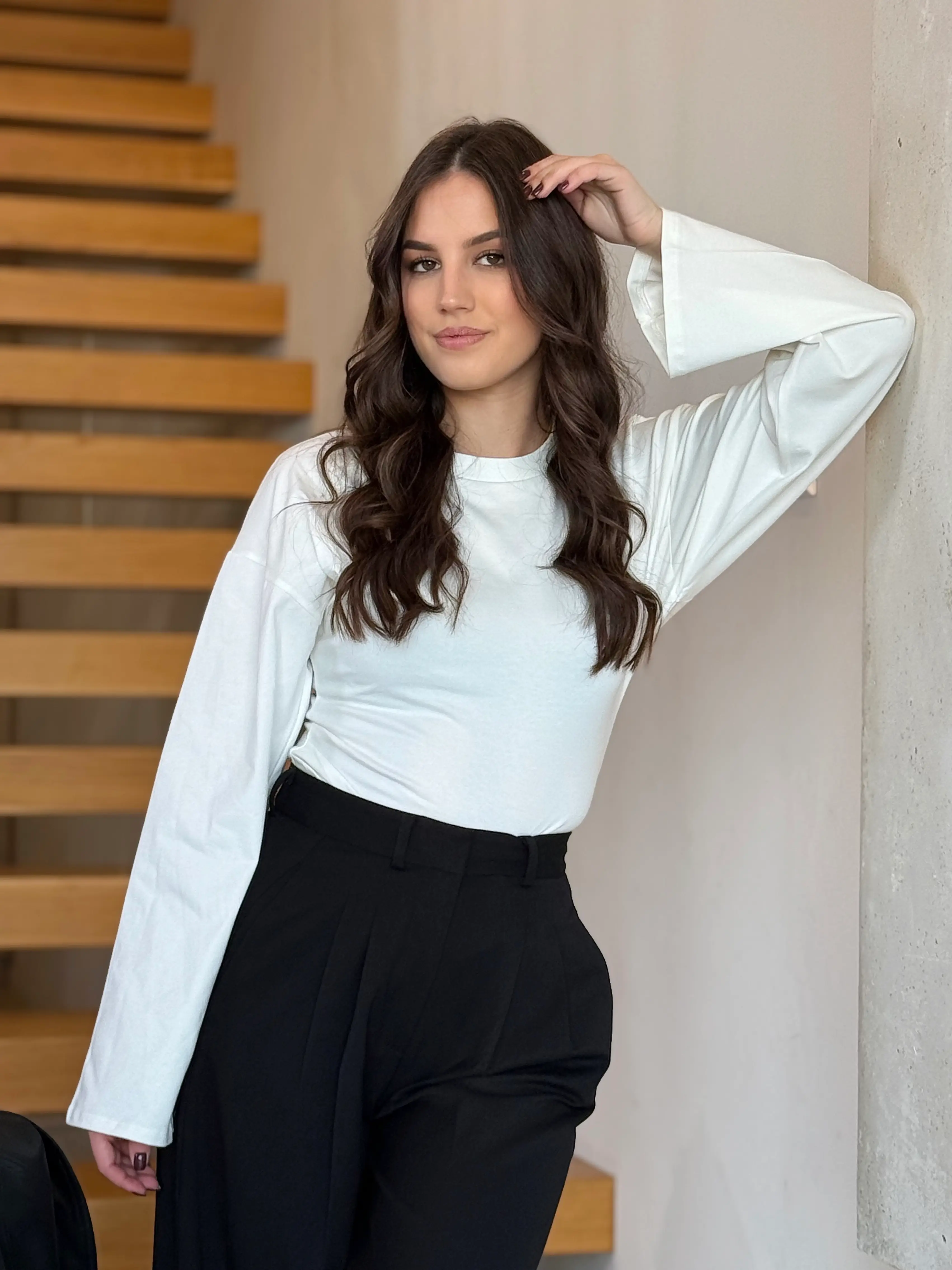 Model nosi žensku bijelu majicu Rosalie pripijenog kroja s dugim širokim rukavima.
