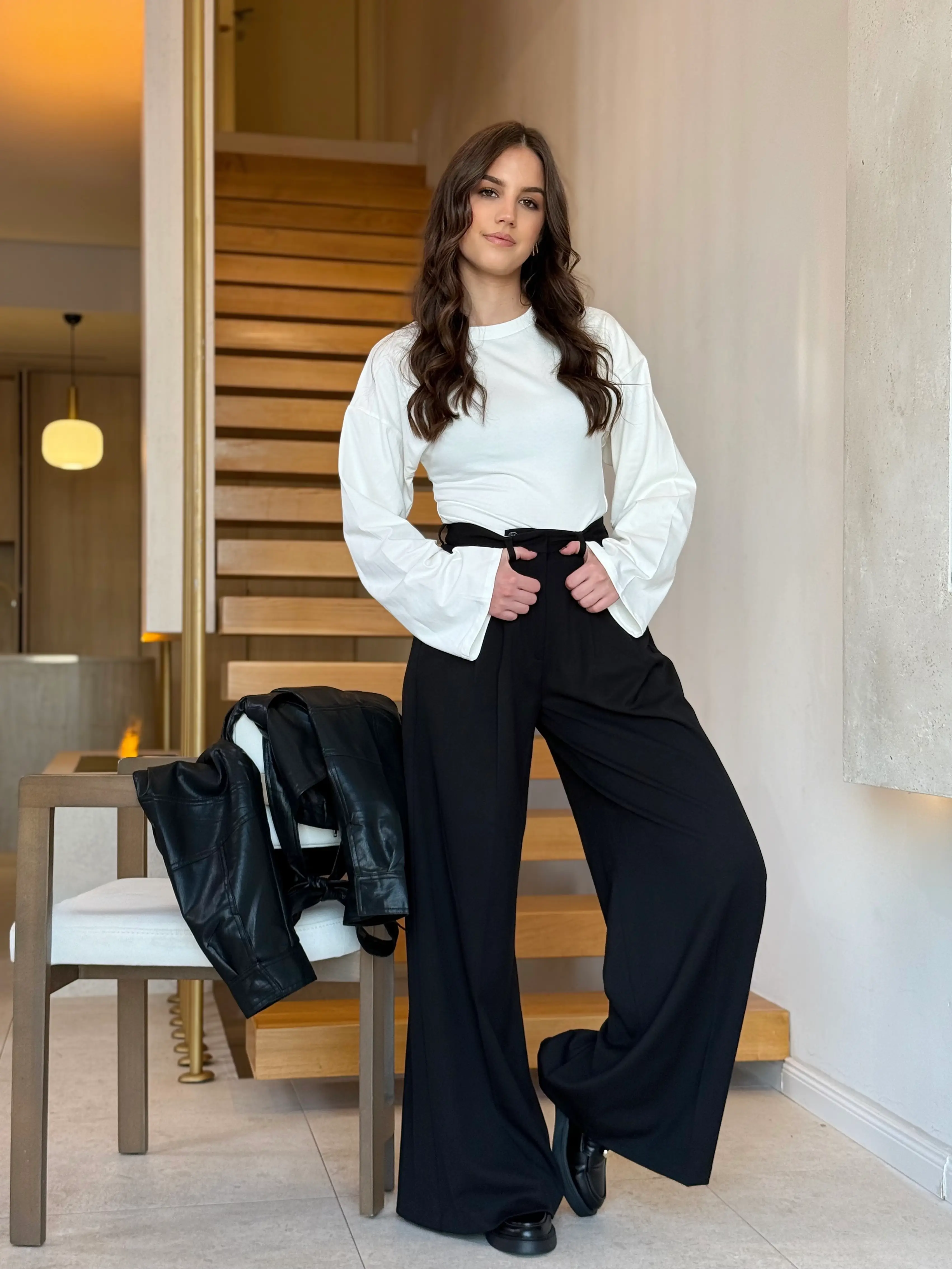 Model nosi ženske crne hlače Marcella visokog struka s dugim širokim nogavicama.